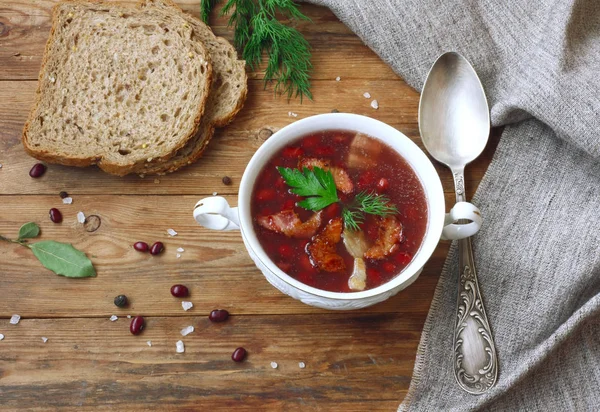 beyaz bir kase, vintage kaşık, baharatlı otlar, ekmek, ahşap masa, rustik tarzı havluda tuval Füme pastırma ile kırmızı fasulye çorbası