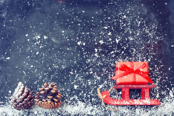 Czerwony Boże Narodzenie Sanie Przenoszenia Pudełko Szyszki Czarnej Powierzchni Śnieg — Zdjęcie stockowe
