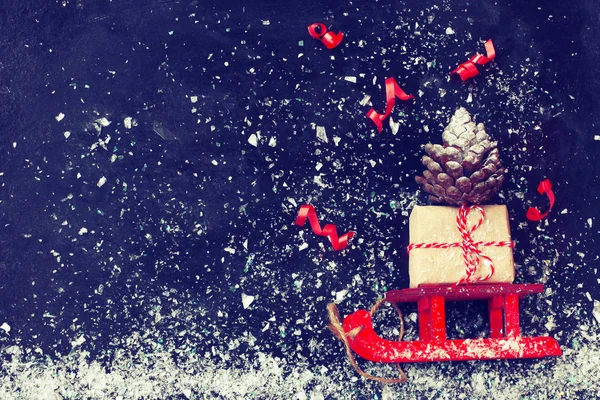 Κόκκινο Χριστουγεννιάτικο Έλκηθρο Που Μεταφέρουν Κουτί Δώρου Κουκουνάρι Ταινία Μαύρη — Φωτογραφία Αρχείου