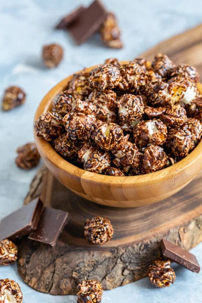 Chocolate caramel popcorn in a bowl and pieces of milk chocolate on a gray concrete background, selective focus.