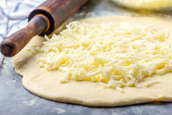 Grated cheese, rolling pin and dough close-up.