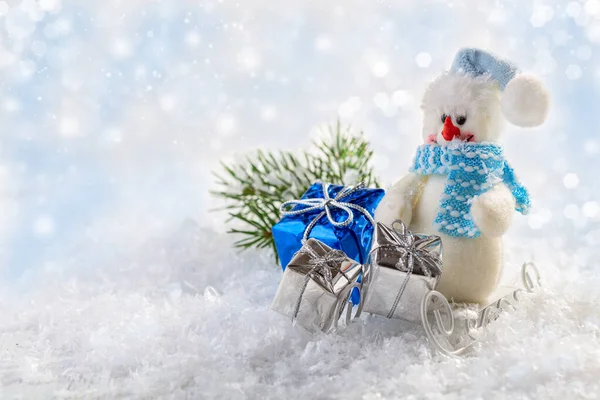 Happy snowman in a blue scarf with gifts on a sleigh. Christmas card with space for text.