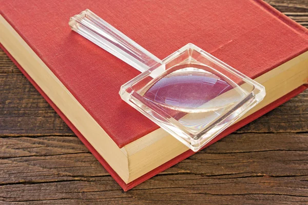 Loupe en verre avec livre sur fond bois — Photo