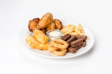 Beyaz tabakta soğan halkaları, kızarmış ekmek, patates kızartması ve tavuk var. Beyaz bir arkaplanda çekilmiş.