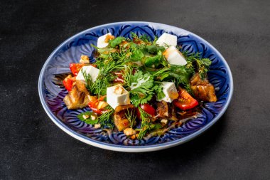 Siyah arka planda patlıcanlı ve taze otlu bir salatanın yakın plan çekimi.