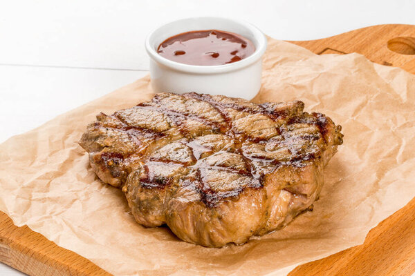 Grilled pork steak with sauce on a wooden board close-up