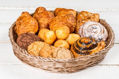 Kruvasan, kurabiyeler, sepette yuvarlanan mermiler beyaz ahşap arka planda yakın plan çekimi.