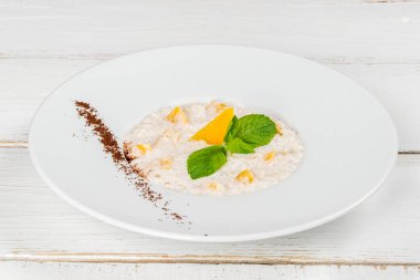 Beyaz bir tabakta nane yapraklarıyla süslenmiş mangolu haşlanmış yulaf ezmesi.