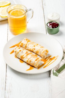 Beyaz yuvarlak tabağa doldurulmuş kahvaltı krepleri. Yakın çekim.