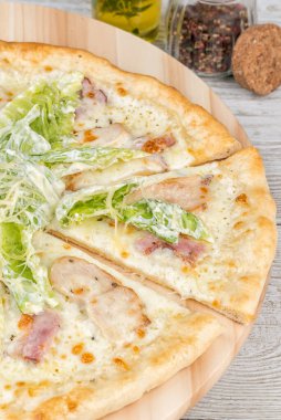 Yuvarlak bir tahtada dilimlenmiş Sezar pizzası. Yakın çekim.