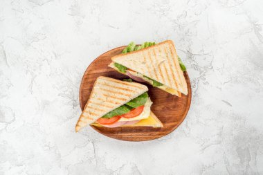 Tahta tabakta peynirli, sosisli, domatesli ve otlu sandviç.