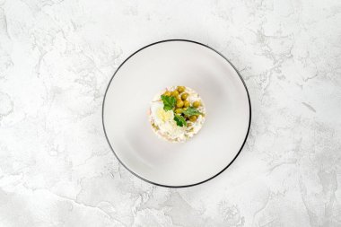 Beyaz yuvarlak tabakta Olivier salatası. Yukarıdan yakın çekim.