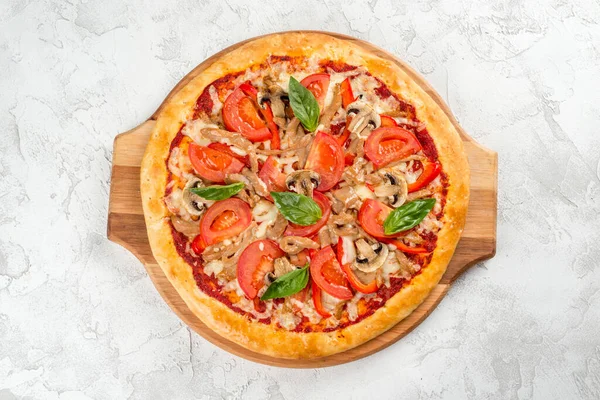 Round pizza with mushrooms and tomatoes on a wooden board