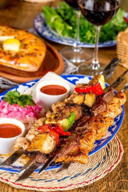 Bir bardak kırmızı şarabın yanında soslu ve sebzeli barbekü.