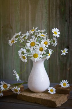 Tahta bir masadaki vazoda bir buket papatya.