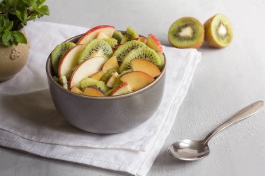 Gri arka planda bir kase meyve salatası. Salatanın bir parçası olarak, armut, elma, erik. 