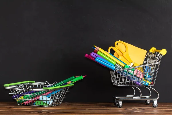 Il concetto di tornare a scuola. Spazio per il testo. Forniture per ufficio in un carrello della spesa su un tavolo di legno vicino alla lavagna — Foto Stock