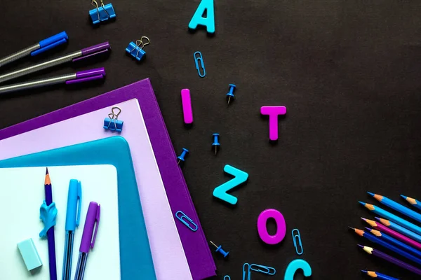 Le concept de retourner à l'école. L'école fournit bleu et violet, cahiers, crayons, stylos, trombones, lettres, boutons sur un fond noir. Espace pour le texte — Photo