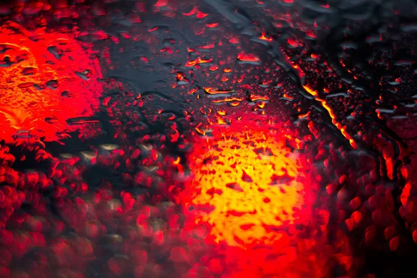 Water drops on the windshield of a car, inside the car when it rains on a city street. Blurred background, red and orange bokeh.