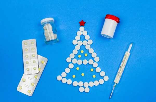 Vista dall'alto di pillole mediche bianche e gialle che formano un albero di Natale, medicinali e un termometro su sfondo blu, il concetto di un Natale medico o felice anno nuovo — Foto Stock