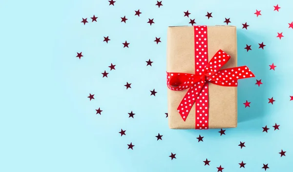 El regalo está envuelto en papel artesanal con una cinta roja sobre un fondo azul. Tarjeta de felicitación de vacaciones. Navidad, Año Nuevo, cumpleaños — Foto de Stock