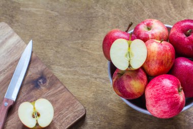Kahvaltı için taze kırmızı elmalar ahşap arka planda kesilmiş bir kesikle bir kasede yatar.