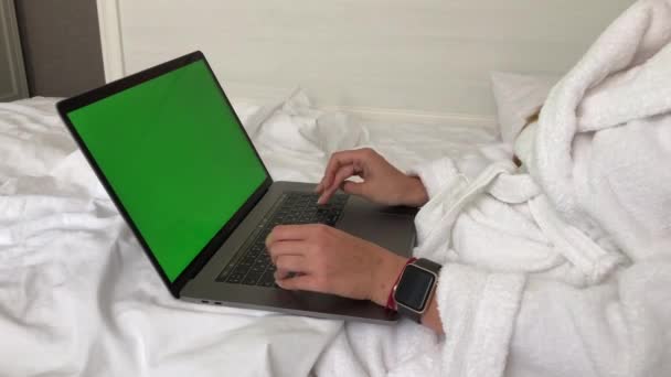 CIUDAD DE MOSCÚ, RUSIA - 10 DE AGOSTO DE 2020: Mujer trabajando en macbook tumbada en la cama en un hotel con albornoz — Vídeo de stock