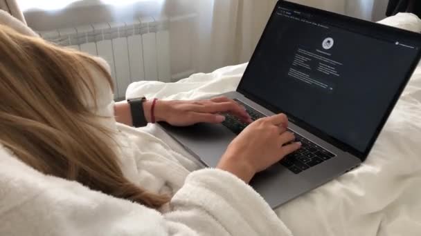 MOSCOW CITY, RÚSSIA - AGOSTO 10,2020: Mulher trabalhando em macbook enquanto estava deitada na cama no hotel em um roupão de banho — Vídeo de Stock