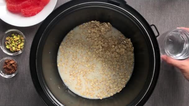 Pour a glass of water into oatmeal with almond milk — Stock Video