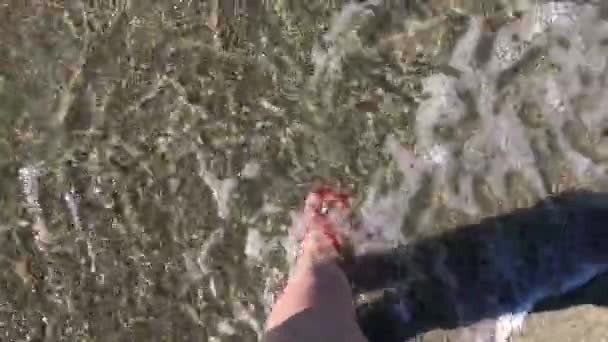 En pige går i flip-flops på stranden og på vandet – Stock-video