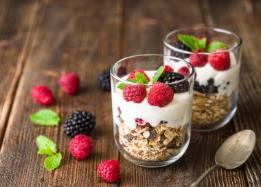 Rustik ahşap arka plan üzerinde beyaz yoğurtlu müsli ve ahududu cam kase.