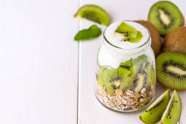 Beyaz yoğurtlu müsli adet kivi sağ tarafındaki üst ve tüm parçaları üzerinde cam kase.