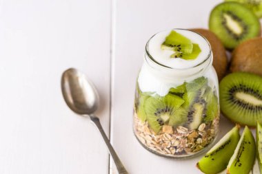 Beyaz yoğurtlu müsli adet kivi sağ tarafındaki üst ve tüm parçaları üzerinde cam kase.