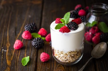 Rustik ahşap arka plan üzerinde beyaz yoğurtlu müsli ve ahududu cam kase.