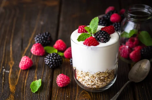 Rustik ahşap arka plan üzerinde beyaz yoğurtlu müsli ve ahududu cam kase.