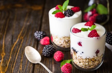 Rustik ahşap arka plan üzerinde beyaz yoğurtlu müsli ve ahududu cam kase.