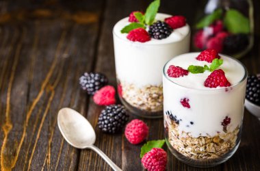 Rustik ahşap arka plan üzerinde beyaz yoğurtlu müsli ve ahududu cam kase.