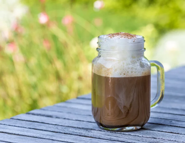 Ice coffee in glass mug with milk and cinnamon on wooden table in the garden.