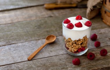 Beyaz yoğurtlu müsli adet ahududu doğal ahşap masa üstüne cam kase..