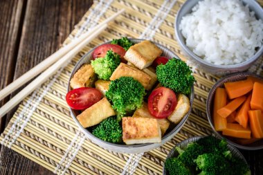 Brokoli ve domates yemek çubuğu sol tarafında bambu yastık üzerinde beyaz kase ile kızarmış tofu.