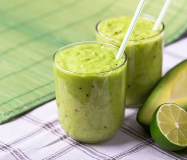 Avokado ve limon sağ tarafındaki yeşil zemin üzerine yeşil smoothie.