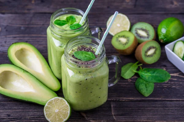 Green smoothie on dark background with avocado, spinach, lemon and kiwi on the right side.