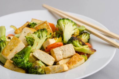 Brokoli ve havuç ile chopsticks sağ tarafındaki beyaz plaka ile kızarmış tofu.
