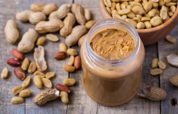 Peanuts butter in small glass cup on natural wooden desk.