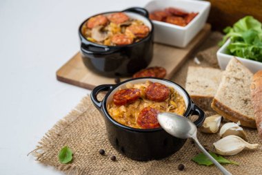 Slovak Noel Ulusal lahana çorbası sosisli Jüt arka plan üzerinde iki küçük siyah tencere.