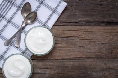 Eski ahşap masa üzerinde beyaz Yoğurtlu iki cam kase.