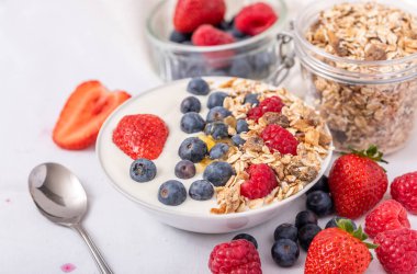 Beyaz arka plan üzerinde yulaf ezmesi ve çilek, yaban mersini ve ahududu ile kase beyaz yoğurt