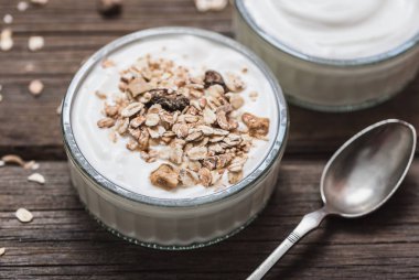 Rustik ahşap masa üstünde yulaf ezmesi ile cam kase beyaz yoğurt.