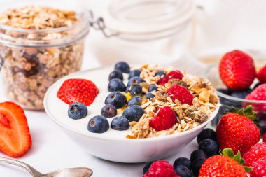 Beyaz arka plan üzerinde yulaf ezmesi ve çilek, yaban mersini ve ahududu ile kase beyaz yoğurt.