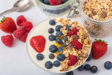 Beyaz arka plan üzerinde yulaf ezmesi ve çilek, yaban mersini ve ahududu ile kase beyaz yoğurt.